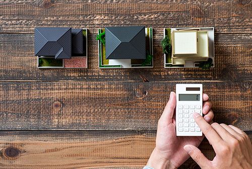 personne tenant une calcultrice au dessus d'un bureau en bois avec des maquettes de maison